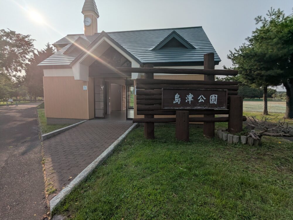 島津公園の入口にある木製看板とログハウス風のトイレ棟