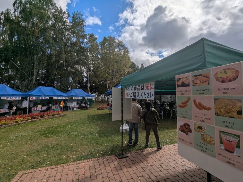 き花の杜 秋の工場祭2026のガーデン。青いテントの屋台と、食券制を案内する看板とメニュー表